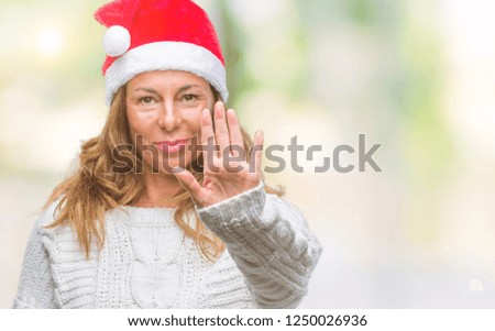 Middle age senior hispanic woman wearing christmas hat over isolated background doing stop sing with palm of the hand. Warning expression with negative and serious gesture on the face.