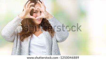 Beautiful plus size young woman wearing winter jacket over isolated background Doing heart shape with hand and fingers smiling looking through sign