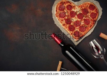 Heart shaped pizza with mozzarella, sausagered with a bottle of wine and wineglas. Valentines day greeting card on rusty background . Top view. Royalty-Free Stock Photo #1250048929