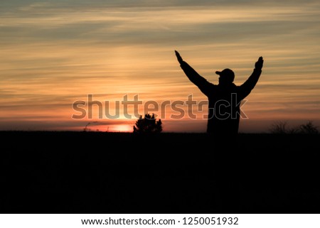 man admiring the red autumn sunset in the field and holding hands raised, the silhouette of a man and a tree
