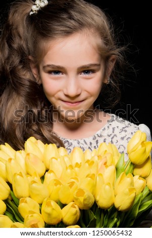 A cute little girl with a bouquet of tulips, in the spring in the studio. The concept of the awakening of nature after winter, the expectation of summer.