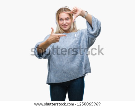 Young caucasian woman listening to music wearing headphones over isolated background smiling making frame with hands and fingers with happy face. Creativity and photography concept.
