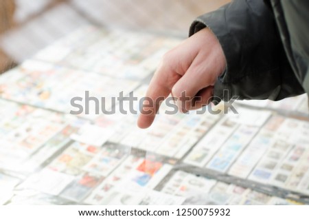 A finger pointing at stamps behind a glass. A man in a warm jacket.