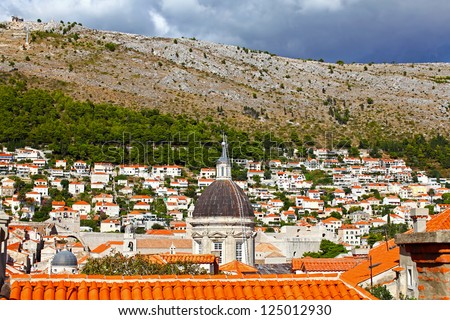 View to the historic wall of Dubrovnik and classic red tiled rooftops of city. Huge mountain over the city in background.