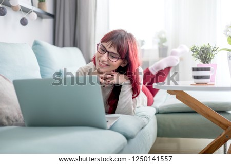 Happy cheerful woman lying on sofa and using laptop at home in bright daylight