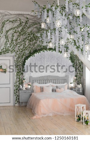 the interior of the bedroom. one double bed. peach blanket. big white tree with flowers in the bedroom. large tree in the interior