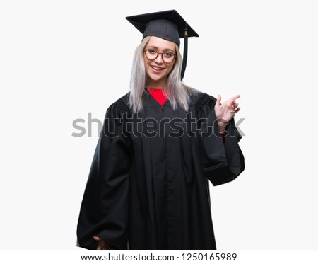 Young blonde woman wearing graduate uniform over isolated background with a big smile on face, pointing with hand and finger to the side looking at the camera.