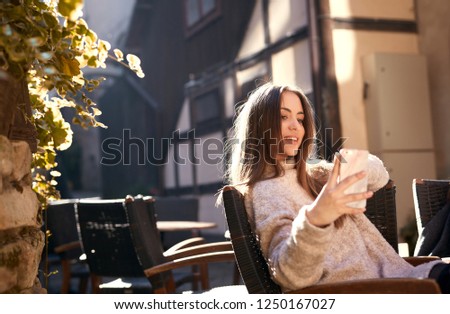 two beautiful cheerful women sitting at the table in the city street cafe at bright sunny spring day. one of the women taking selfie