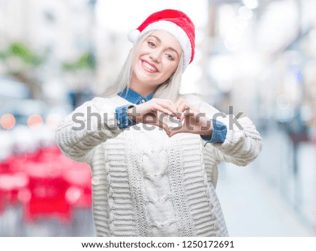 Young blonde woman wearing christmas hat over isolated background smiling in love showing heart symbol and shape with hands. Romantic concept.