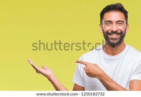 Adult hispanic man over isolated background amazed and smiling to the camera while presenting with hand and pointing with finger.