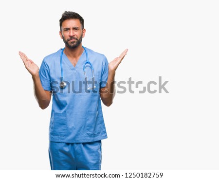 Adult hispanic doctor or surgeon man over isolated background clueless and confused expression with arms and hands raised. Doubt concept.