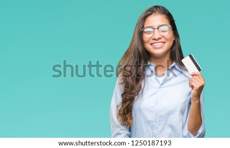 Young arab woman holding credit card over isolated background with a happy face standing and smiling with a confident smile showing teeth