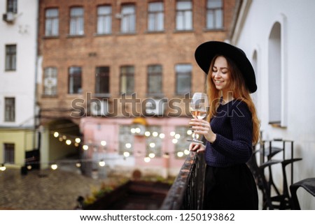Woman stay on balcony and drink some wine. Pretty smiling woman with glass of wine. Holiday vibes and mood