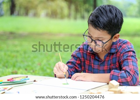 Boy in 12years old with eyeglasses have concentrate with hand paint watercolor picture with green park background, child education concept.