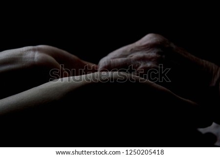 Silhouettes of old hands of grandmother and granddaughter in the rays of light on a dark background