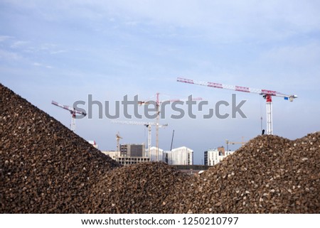 Stock photo of cranes at construction site, behind piles of gravel. 