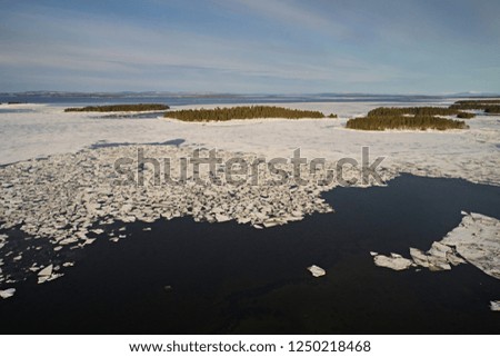 Aerial view of the archipelago and the sea, with a partially frozen water surface against a blue sky during the daytime. Beautiful winter landscape with the islands of the northern country with drone.