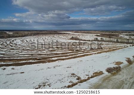 Aerial view of winter fields under the snow against a blue sky and clouds. Landscape with drone on a bright sunny day