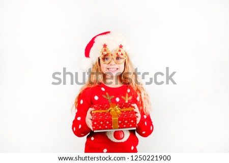 Close up portrait cute and funny blond little girl holding Christmas present in colorful festive wrapping, tied with golden ribbon on isolated background with copy space. Christmas mood concept.