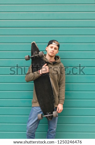 Portrait of a teenager in casual clothing with a skate in his hands against the background of a turquoise wall. Skate Concept. Street culture.