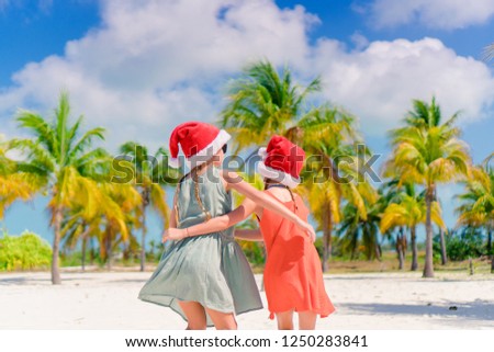 Little adorable girls in Santa hats during beach Christmas vacation having fun together