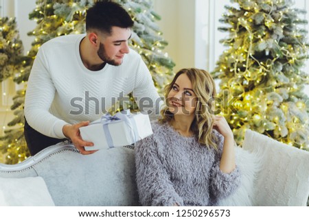 The guy gives a gift to the girl on the background of the Christmas tree. Christmas background

