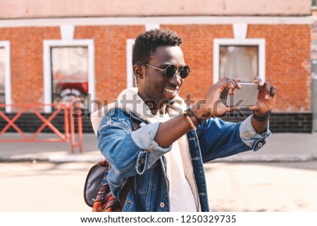 Cheerful smiling african man taking selfie picture by smartphone walking on city street