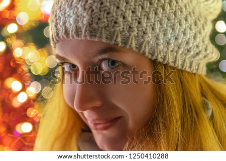 Pretty woman in white knitted hat with pompon is walking on the evening streets of big city and rejoicing at coming winter in christmas mood.