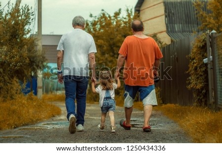 A little blond girl in the middle and two grown mans walking on the country street after rain. She is in safe hands.