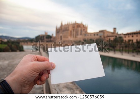 White postcard mockup in man's hand on the background Catedral de Mallorca in Palma town on Mallorca Island in Spain