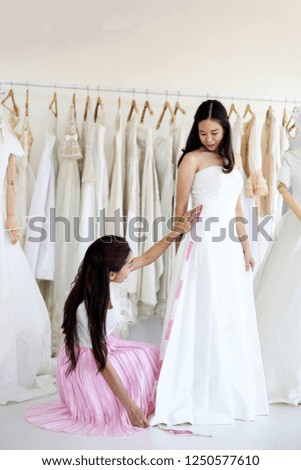 Beautiful bride getting dressed by her best friend in her wedding day and choosing a wedding dress in the shop and the shop assistant is helping her