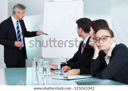 Bored businesswoman sleeping in a meeting as her colleague who is giving the presentation talks in the background