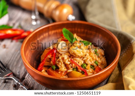 Concept of Spanish cuisine. Paella with seafood and shrimps, with green peas in a clay plate. A glass of cool wine is on the table.