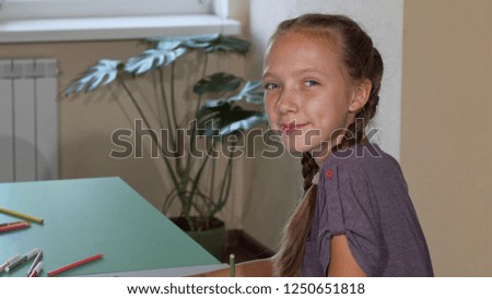 Happy cute schoolgirl smiling to the camera over her shoulder while drawing