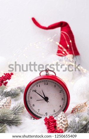 Red  alarm clock - symbol of  New Year, fir tree branches, berries,  gnome, balls  on white fur background. Winter holidays concept. Time concept. Vertical image.
