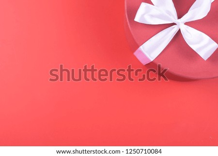 Round gift box with tied up with cute white silky ribbon with a bow on vibrant red background with copy space for text. Holiday and surprising concept.