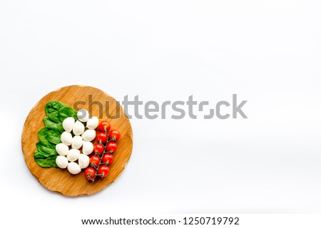 Italian flag made of mozzarella cheese, cherry tomatoes, green basil on wooden cutting board on white background top view copy space