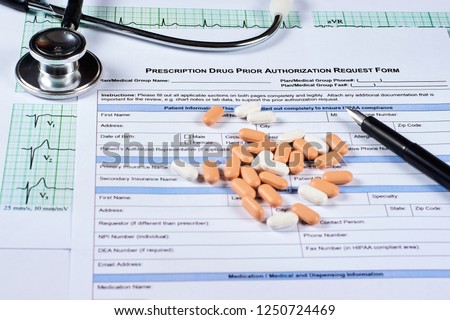 Prescription drugs prior authorization request form, pills, stethoscope and pen on a EKG graph paper background. Close-up. Royalty-Free Stock Photo #1250724469