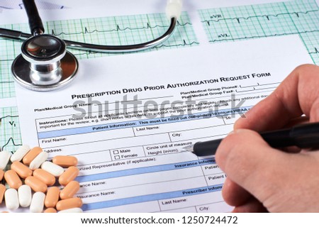 Human fill Prescription drugs prior authorization request form, pills, stethoscope on a EKG graph paper background. Close-up. Royalty-Free Stock Photo #1250724472