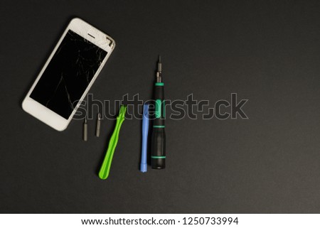 Broken white phone with repair tools kit on the dark background
