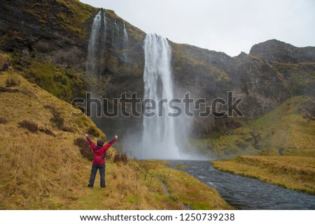 Tourist lady rise two hand up in happy position at Seljalandsfoss waterfall in Iceland winter.