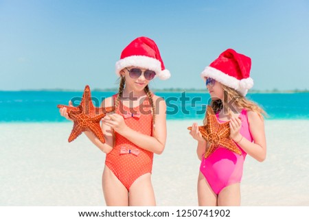 Little girl in Christmas hat on white beach during Xmas vacation with starfish