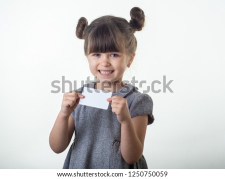 Cute smiling child with glasses holding discount white card in her hands. Kid with credit card. Little girl showing empty blank paper note copy space.
