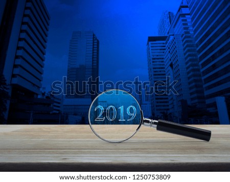 Magnifying glass with 2019 text and graph on wooden table over number and modern office city tower, Business happy new year research concept
