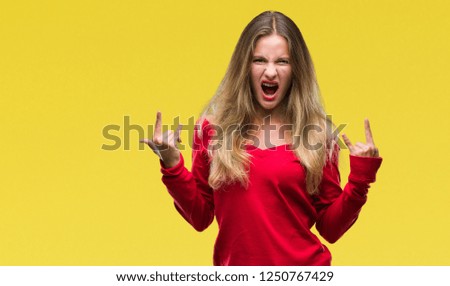 Young beautiful blonde woman wearing red sweater over isolated background shouting with crazy expression doing rock symbol with hands up. Music star. Heavy concept.