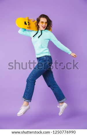 Image of an amazing happy young woman posing isolated over purple background wall holding skateboard.