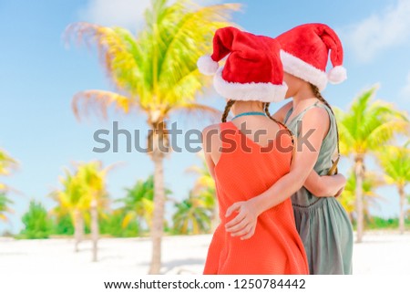 Little adorable girls in Santa hats on beach Christmas vacation having fun together. Back view of two kids on New Year