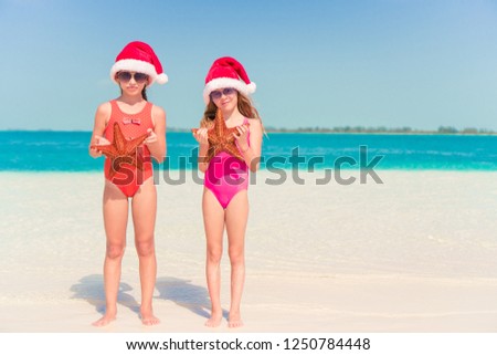 Little girls in Christmas hat on white beach during Xmas vacation with starfish in hands