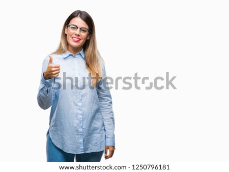 Young beautiful business woman wearing glasses over isolated background doing happy thumbs up gesture with hand. Approving expression looking at the camera with showing success.