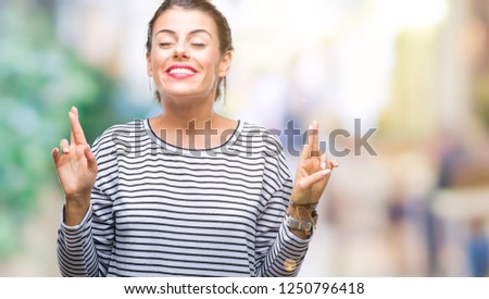 Young beautiful woman casual stripes sweater over isolated background smiling crossing fingers with hope and eyes closed. Luck and superstitious concept.
